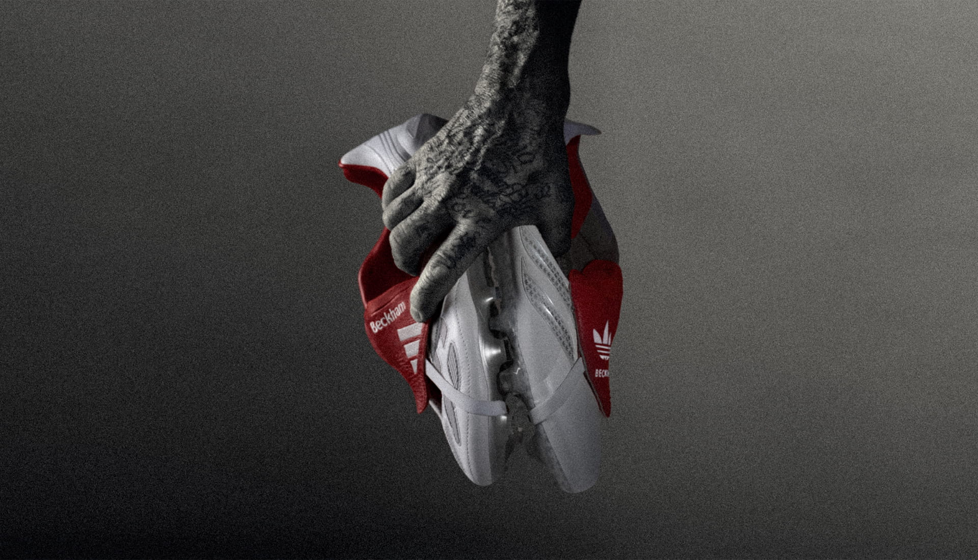 Mano sosteniendo botines adidas blancos con detalles rojos